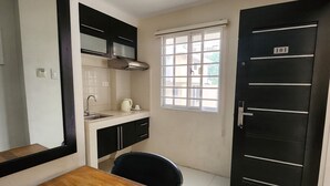 A compact kitchen with a wooden dining table, a black chair, a window with blinds, and a black door with the number 101.