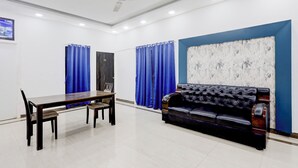 A room with a dining table and chairs, a black leather sofa, blue curtains, and a ceiling fan. - Fabhotel Ravana Kottai (Chennai)