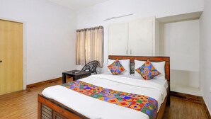 A bedroom with a wooden bed, white curtains, a small table, and a wardrobe. - Fabhotel Ravana Kottai (Chennai)