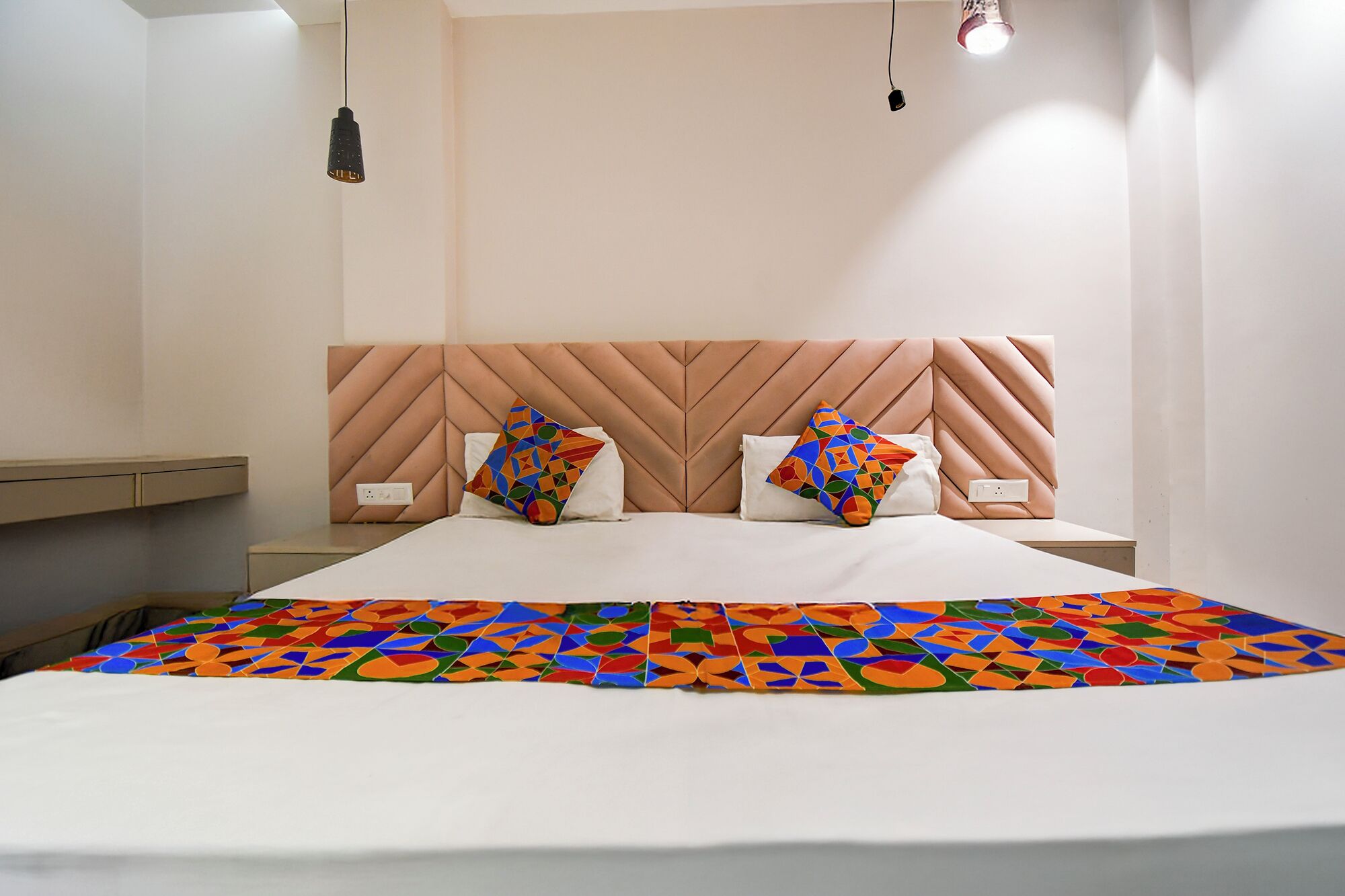 Un lit bien fait, recouvert d’une couvre-lit aux motifs géométriques colorés, avec une tête de lit à chevrons et deux lampes de chevet.