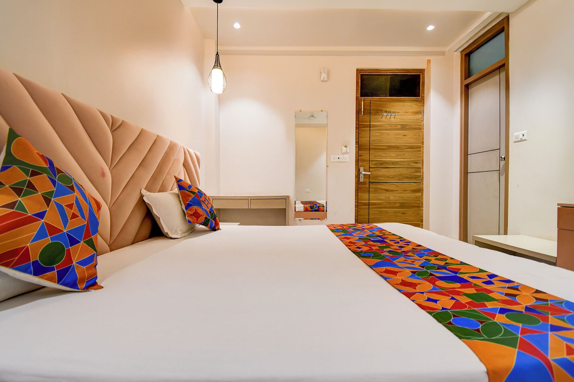 A hotel room with a large bed, a wooden wardrobe, a mirror, and a hanging light fixture.