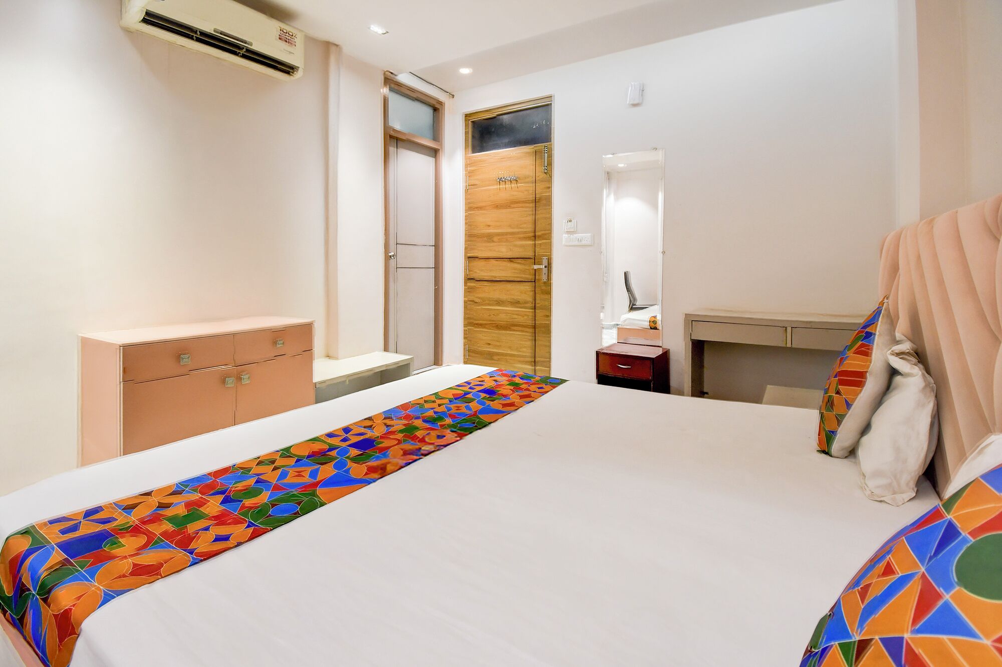 Une chambre à coucher comprenant un lit, une commode, une coiffeuse avec un miroir et une porte donnant sur une autre pièce.