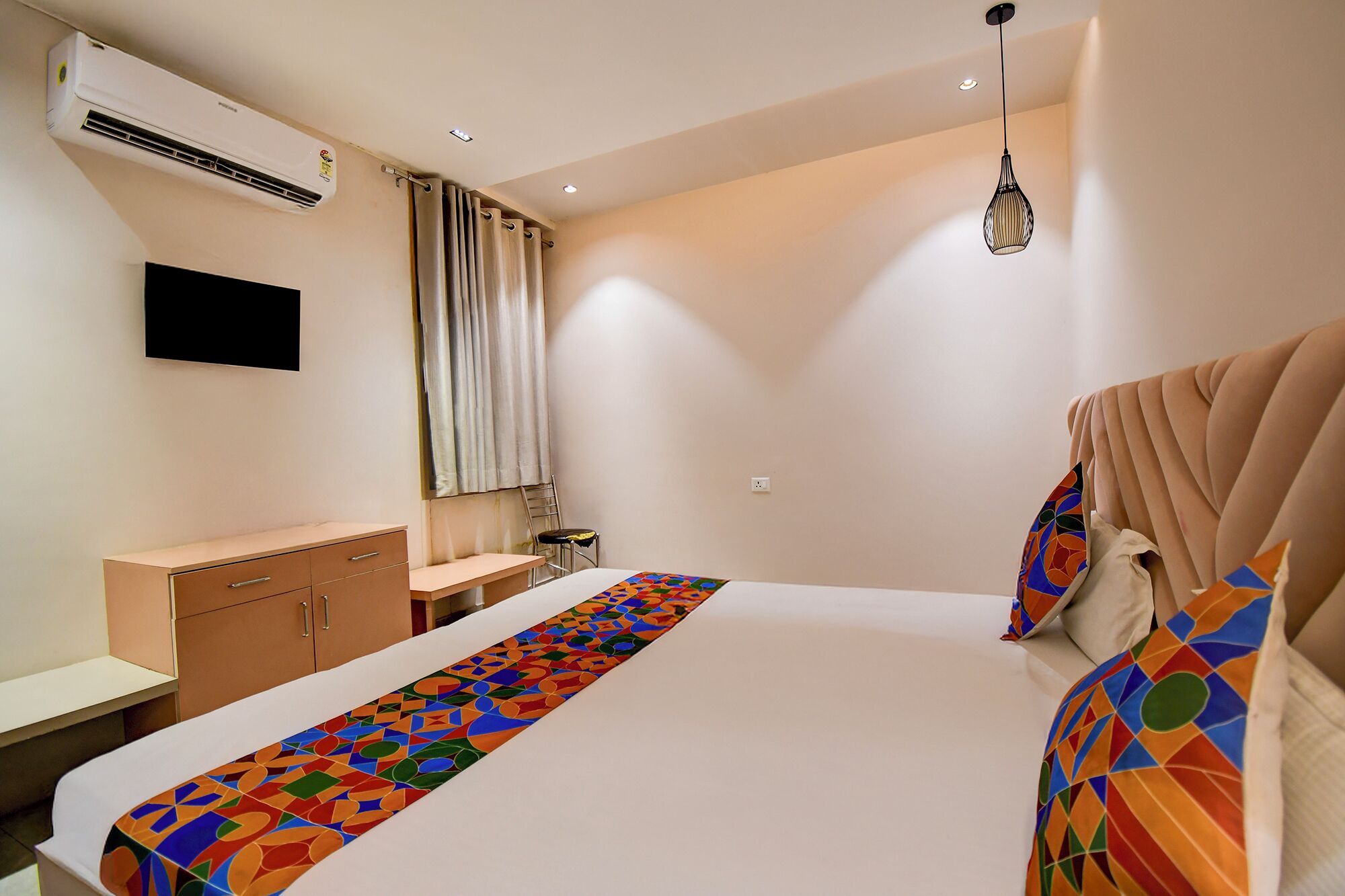 Habitació d'hotel moderna amb un llit gran, una taula de treball, una cadira, un aparell d'aire condicionat i un penjador amb llum.