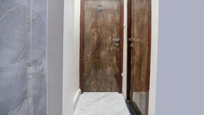 A hallway with a wooden door labeled 203, a marble floor, and a glass door on the right. - Fabhotel B Town (Mumbai)