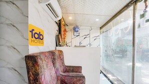 A hotel reception area with a marble wall, a sign for 'fab hotels', a patterned sofa, and a large window with blinds. - Fabhotel B Town (Mumbai)