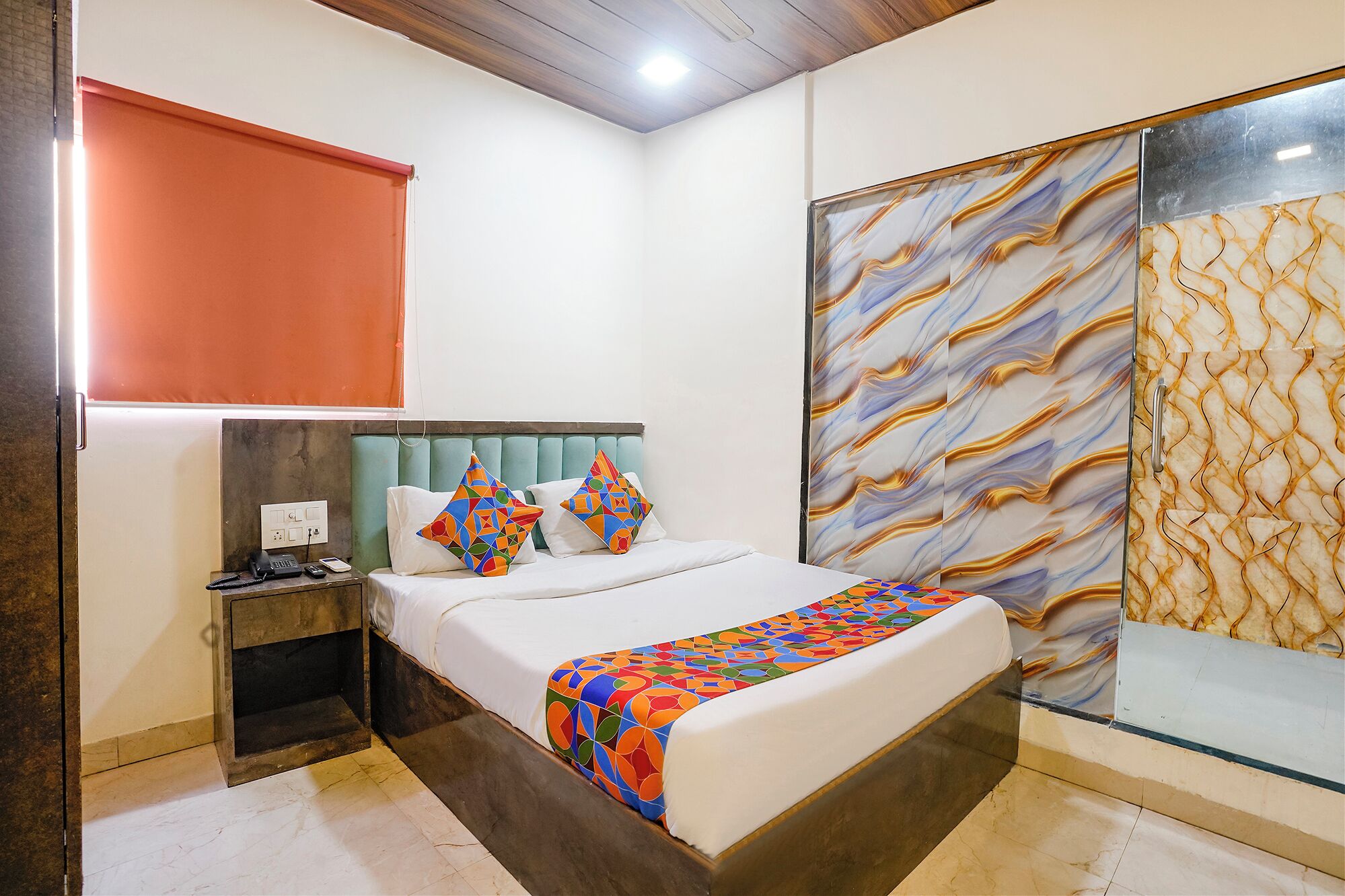 A hotel room with a bed, a nightstand, a telephone, and a window with a patterned curtain.