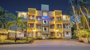 A multi-story hotel with balconies, a central entrance, and a well-lit facade. - Fabhotel Charvi Reemz (Anjuna)