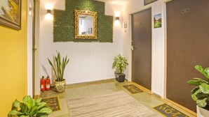 A hotel lobby with a green wall, a mirror, potted plants, and a fire extinguisher. - Fabhotel Charvi Reemz (Anjuna)