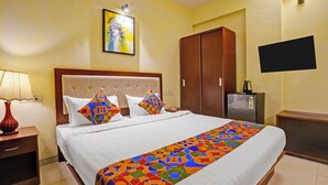 A hotel room with a bed, a nightstand, a lamp, a wardrobe, a television, and a painting on the wall. - Fabhotel Charvi Reemz (Anjuna)