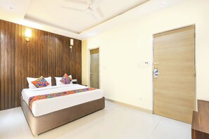 A hotel room with a bed, wooden panel wall, ceiling fan, and a door. - Fabhotel Outstay (Navi Mumbai)