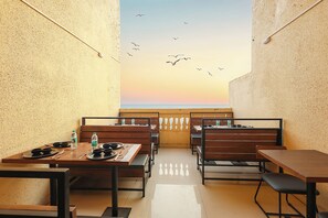 An outdoor dining area with wooden benches and tables, a view of the sky, and a railing. - Fabhotel Outstay (Navi Mumbai)