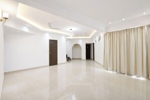 A spacious, well-lit hallway with a modern ceiling design, a chandelier, and a large window with curtains. - Fabhotel Outstay (Navi Mumbai)