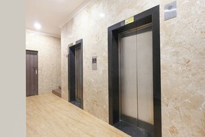 A hallway with two elevators, marble walls, and a wooden floor. - Fabhotel Outstay (Navi Mumbai)