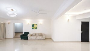 A spacious living area with a high ceiling, a ceiling fan, a green armchair, a beige sofa, and a staircase leading to an upper level. - Fabhotel Outstay (Navi Mumbai)