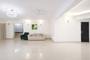 A spacious living area with a high ceiling, a ceiling fan, a green armchair, a beige sofa, and a staircase leading to an upper level. - Fabhotel Outstay (Navi Mumbai)
