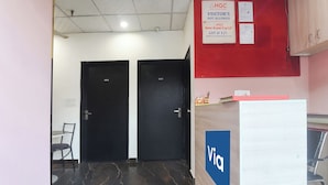 A hotel reception area with a blue sign reading 'Viva,' two black doors labeled '001' and '002,' and a red wall with signs indicating hotel policies and GST. - Via Capitol Square (Jaipur)