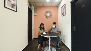 A room with a round table, two chairs, a ceiling fan, and a clock on the wall. - Via Capitol Square (Jaipur)
