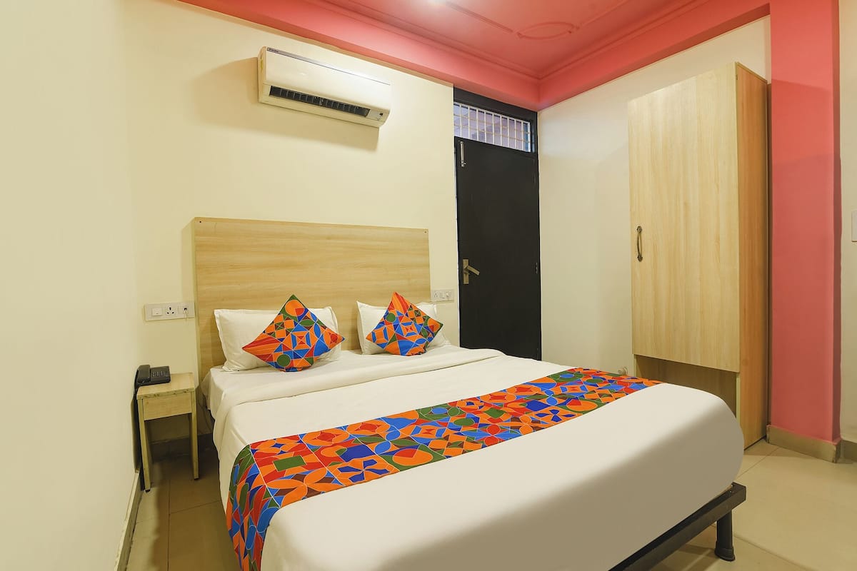 Una habitación de hotel con cama, mesita de noche, unidad de aire acondicionado, armario y una puerta con ventana.