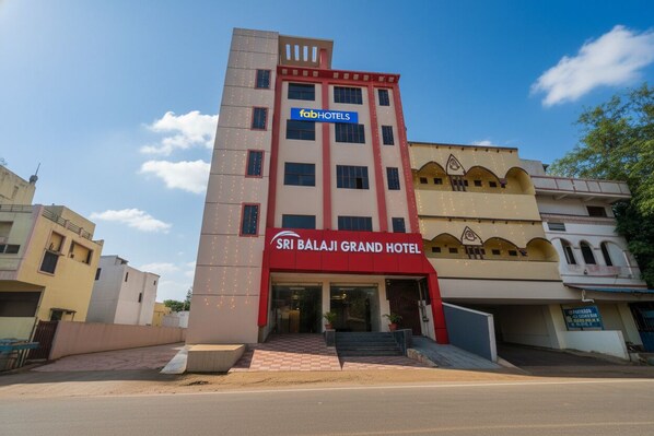 Egy többemeletes szálloda, feltűnő vörös és bézs színű homlokzattal, melyen a „Sri Balaji Grand Hotel” és a „FabHotels” felirat is látható.
