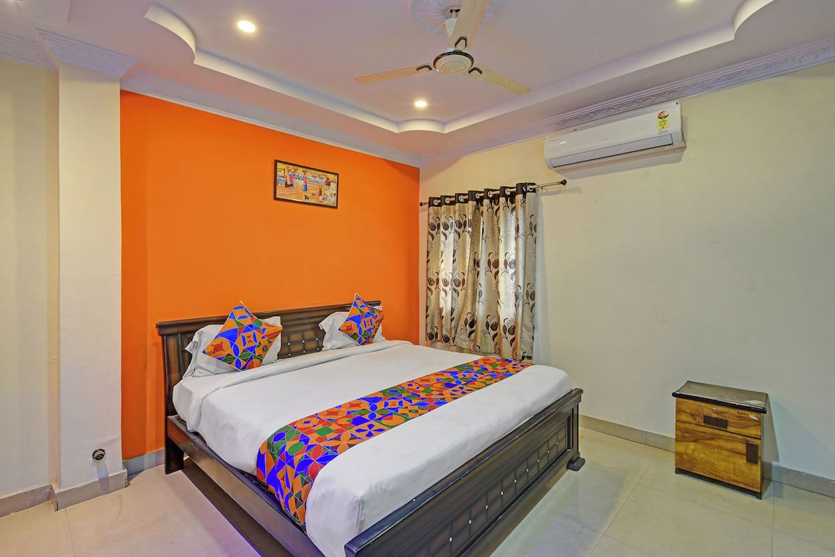 A bedroom with a bed, an air conditioner, a ceiling fan, and a small wooden cabinet.