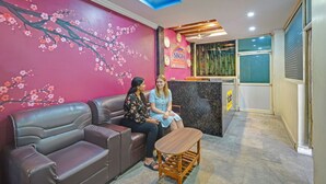 A reception area with a pink wall, a wooden reception desk, and a seating area with a brown sofa and a small wooden table. - Fabhotel Sri Balaji Grand (Hyderabad)