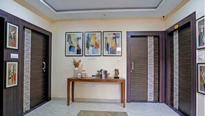 A hallway with a wooden console table, framed abstract art, and two dark wooden doors. - Fabhotel Shri Vishwanath (Varanasi)
