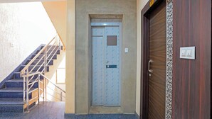 A building entrance with a staircase leading to an upper floor, a door with a metal handle, and a wall-mounted light switch. - Fabhotel Shri Vishwanath (Varanasi)