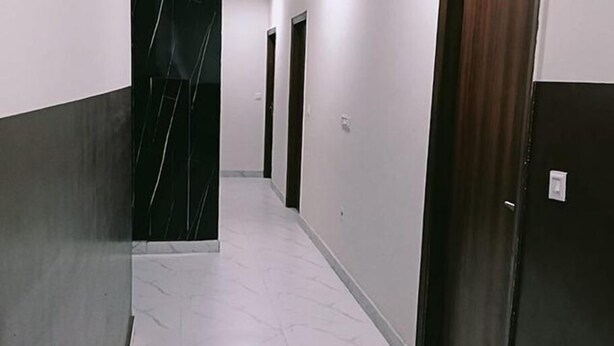 A hallway with a marble floor, a dark door on the right, and a black door at the end. - Fabhotel Vedika (Kolkata)
