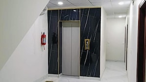 A hallway with a marble wall, a fire extinguisher, and an elevator. - Fabhotel Vedika (Kolkata)
