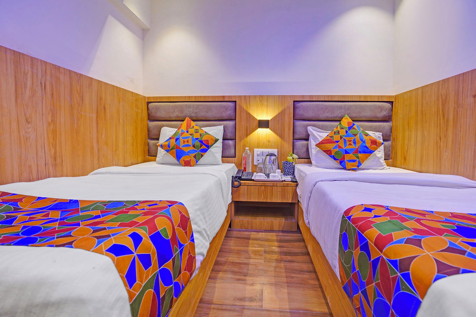 A hotel room with two beds, wooden headboards, and colorful geometric-patterned bedspreads.