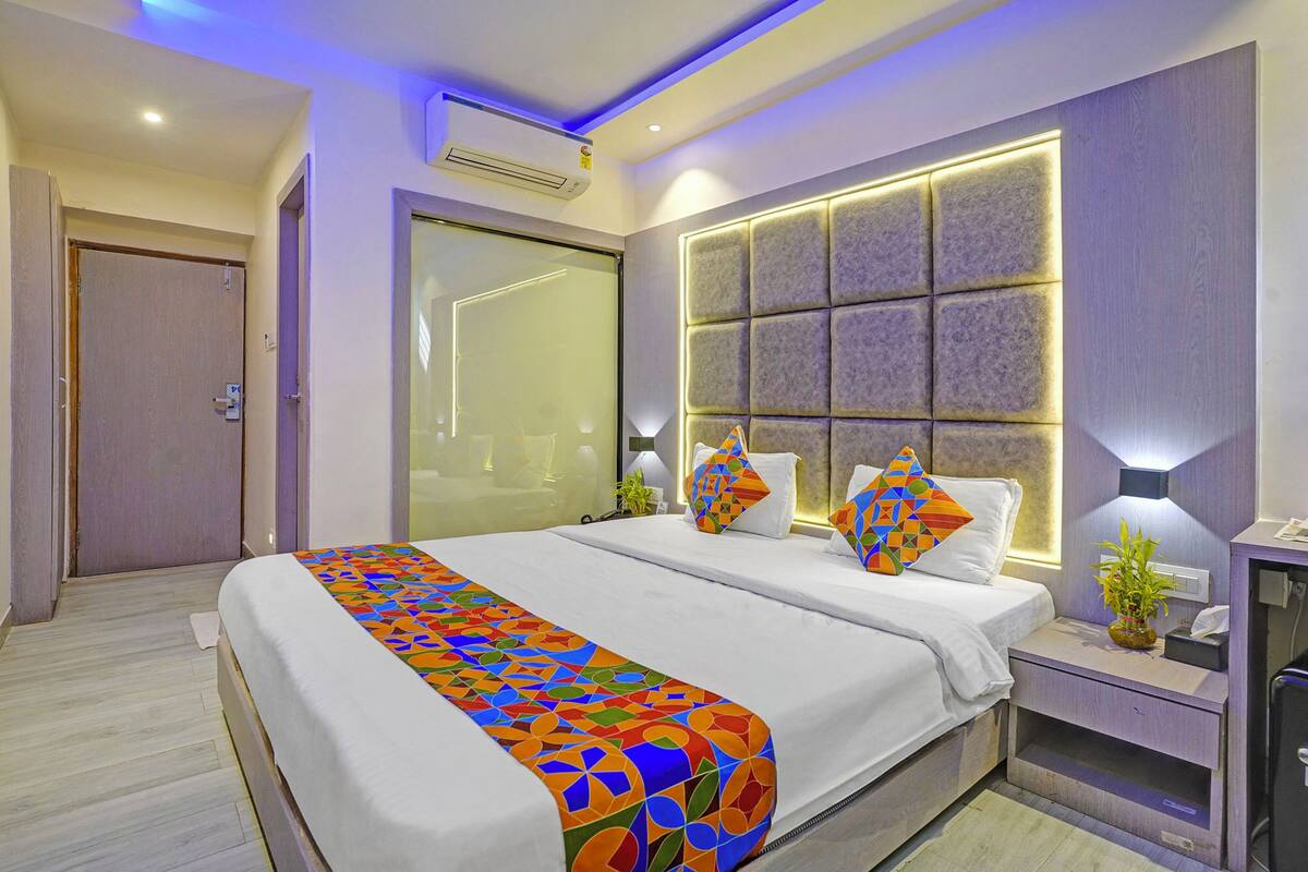 Una habitación de hotel moderna con una cama grande, una mesita de noche con lámpara y un equipo de aire acondicionado instalado en la pared.
