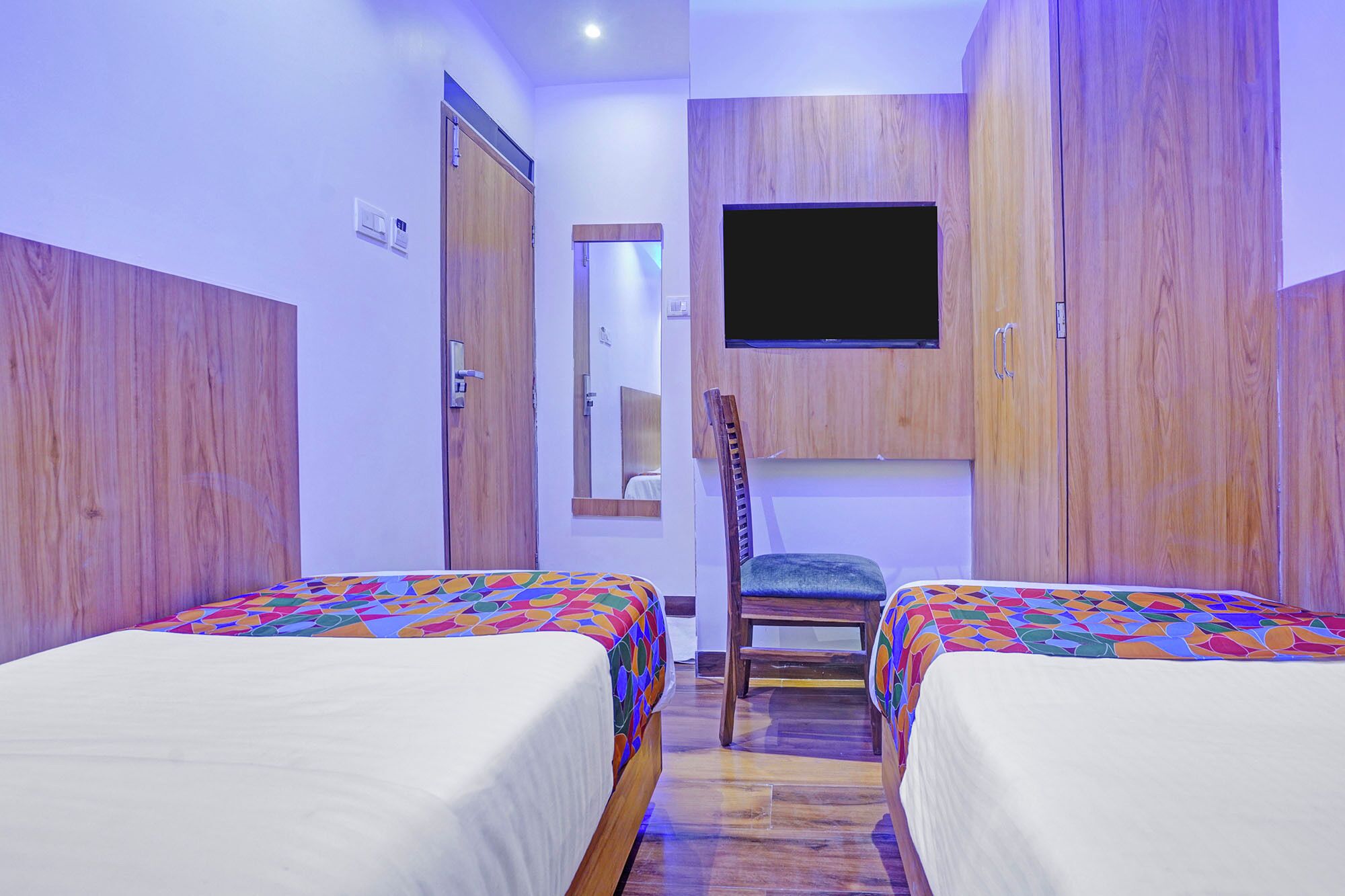 A bedroom with two beds, a TV mounted on the wall, and wooden wardrobes.