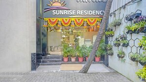 Der Eingang von Sunrise Residence mit einem Schild, Blumentöpfen und einem gefliesten Weg.