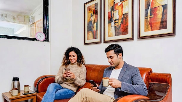A couple sitting on a leather couch with abstract paintings on the wall, a coffee table with a coffee maker, and a clock on the wall. - Via RK Exclusive (Hinjawadi)