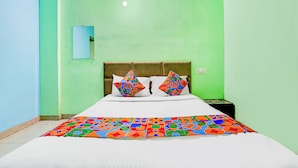 A hotel room with a bed, two pillows, a nightstand, and a wall-mounted light. - Via RK Exclusive (Hinjawadi)