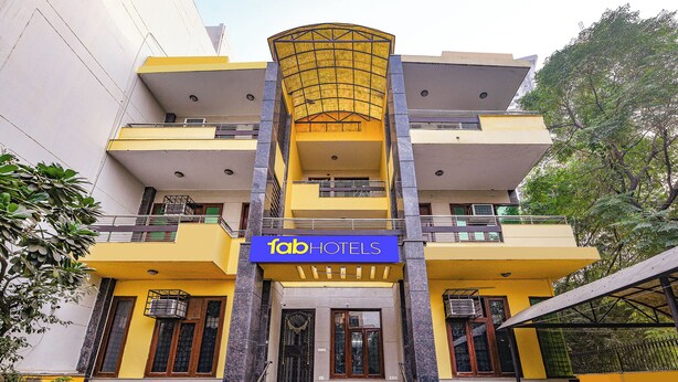 A multi-story building with a prominent yellow facade, a blue sign reading "fabHOTELS", and a central entrance with steps leading up to a door. - Fabhotel Uk House Residency (Gurugram)