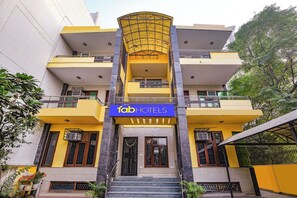 Un edificio a più piani con una facciata gialla ben visibile, un cartello blu con la scritta "fabHOTELS" e un ingresso centrale con gradini che portano a una porta.