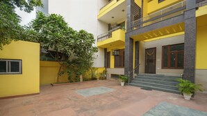 A multi-story building with a yellow facade, a staircase leading to the entrance, and potted plants around the courtyard. - Fabhotel Uk House Residency (Gurugram)