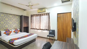 A hotel room with a bed, a desk, a chair, a wardrobe, a ceiling fan, an air conditioning unit, and a window with curtains. - Fabhotel Ramraj Inn (Chhatrapati Sambhajinagar)