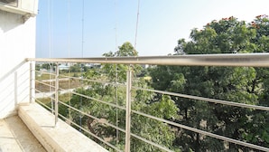 A balcony with a metal railing overlooking a garden with trees and a clear sky. - Fabhotel Ramraj Inn (Chhatrapati Sambhajinagar)