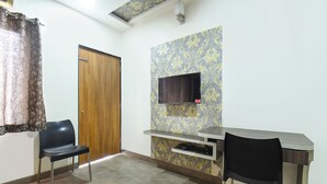 A small, private room with a wooden door, a flat-screen TV mounted on the wall, two chairs, and a desk. - Fabhotel Ramraj Inn (Chhatrapati Sambhajinagar)