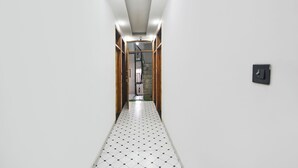 A hallway with a tiled floor, a wooden door frame, and a light switch on the wall. - Fabhotel The Dream Inn (Faridabad)
