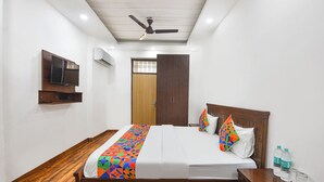A hotel room with a wooden bed, a TV mounted on the wall, and a ceiling fan. - Fabhotel The Dream Inn (Faridabad)