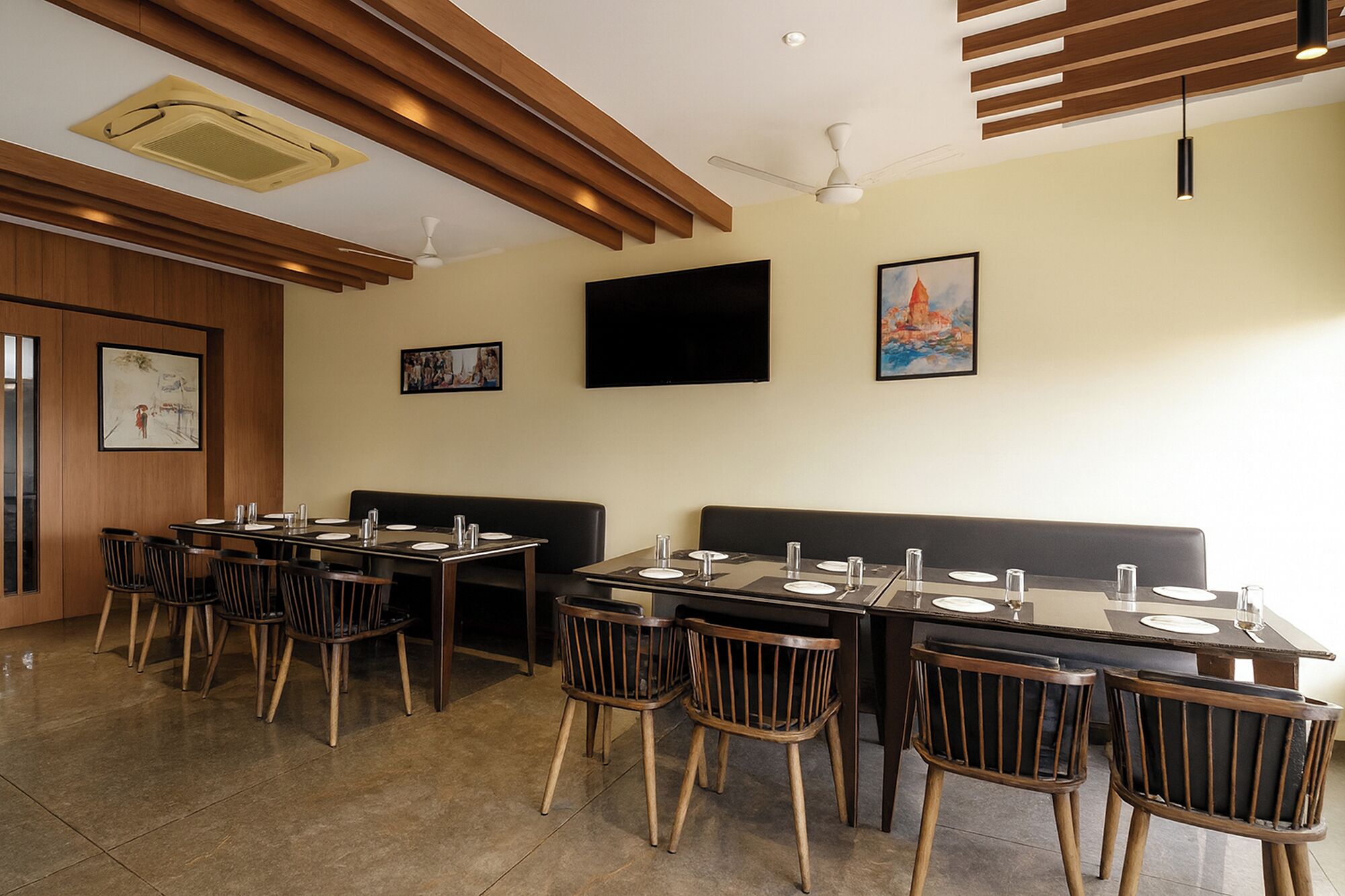 A restaurant with wooden ceiling beams, a flat-screen TV, and artwork on the walls.