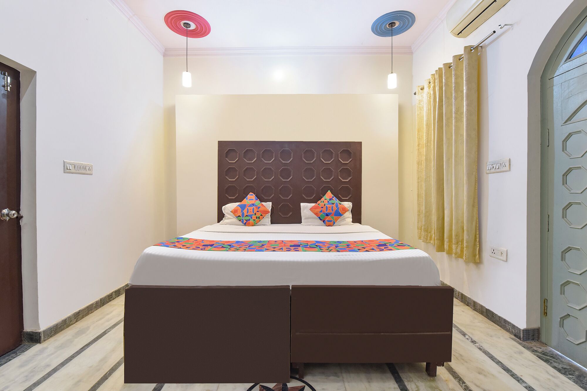 A hotel room with a bed, a headboard with hexagonal patterns, a patterned bedspread, and a door with a geometric design.