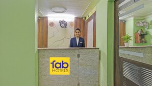 A hotel reception area with a marble counter, a clock, and a fan on the wall. - Fabhotel Akki Residency 66 (Noida)