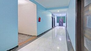 A hallway with light blue walls, a fire extinguisher mounted on the wall, and a door at the end. - Fabhotel Akki Residency 66 (Noida)
