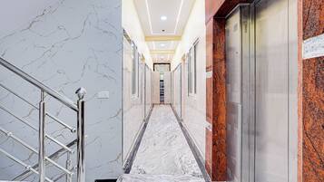 A marble-floored hallway with a metal railing, leading to a door with a red granite accent wall.