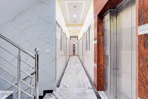 A marble-floored hallway with a metal railing, leading to a door with a red granite accent wall. - Via Golden Inn I (Bengaluru)