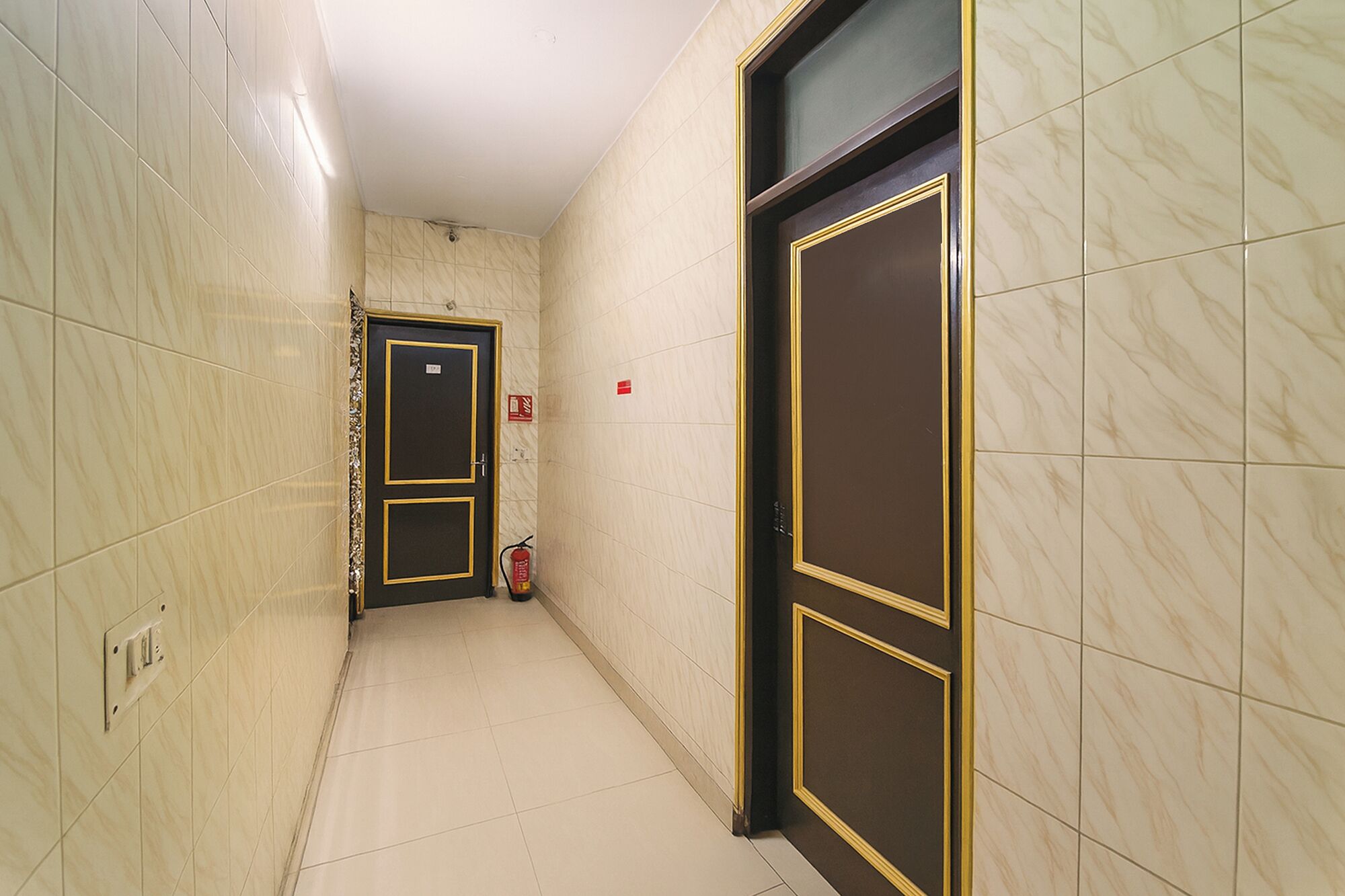 A corridor with marble walls and doors, a fire extinguisher, and a light switch on the wall.